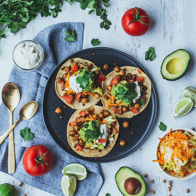 Vegan tacos with fresh greens and a side of spicy salsa on a wooden table.